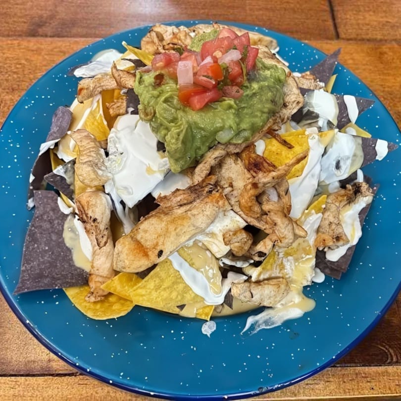 A blue plate of nachos topped with chicken, guacamole, pico de gallo, and sour cream.